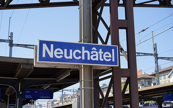 Un cartello ferroviario con scritta bianca su sfondo blu riporta il nome della stazione di Neuchâtel. 